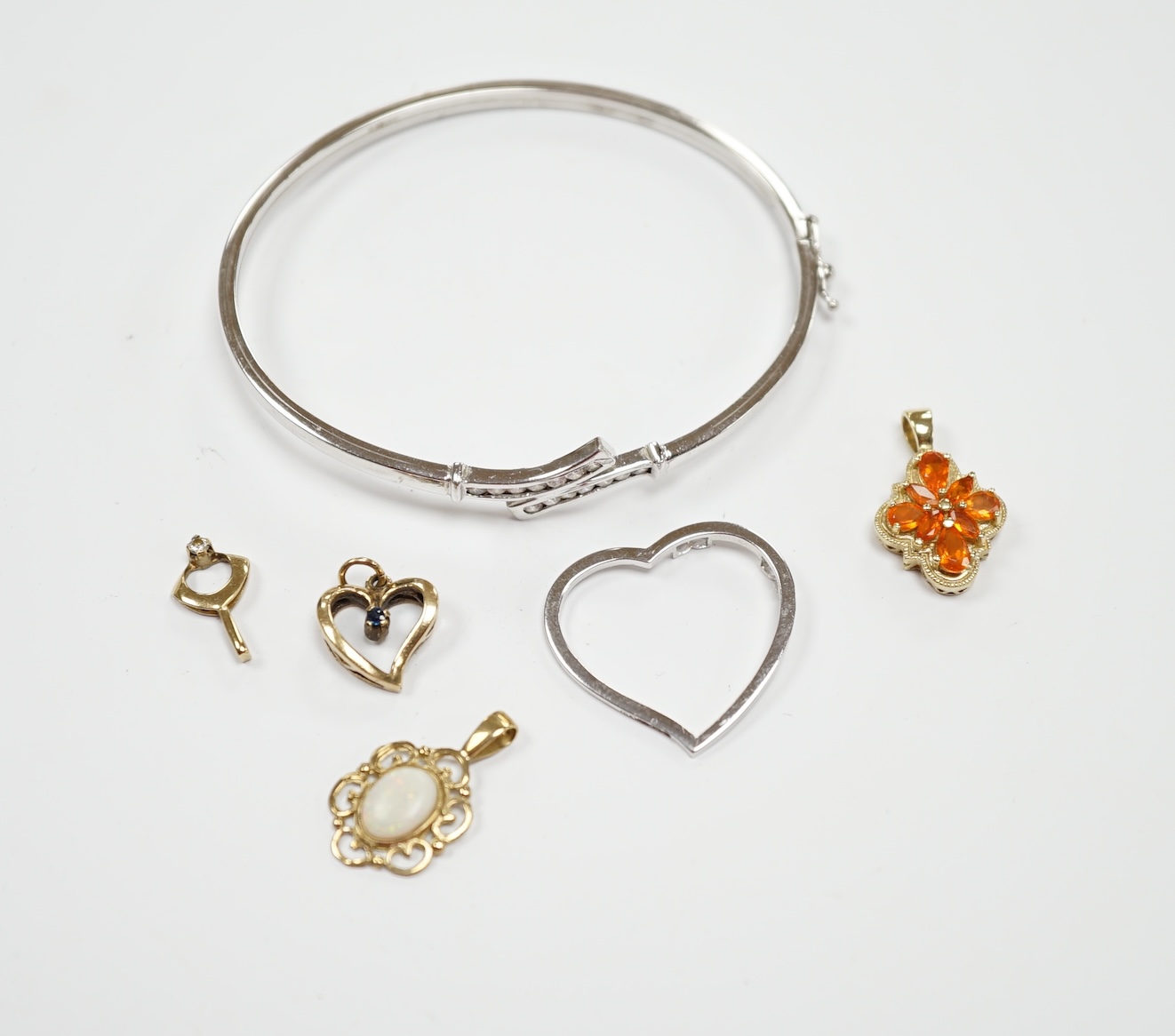 A 9ct white gold heart pendant, a 9kt bangle, two 9ct and gem set pendants and two yellow metal pendants.